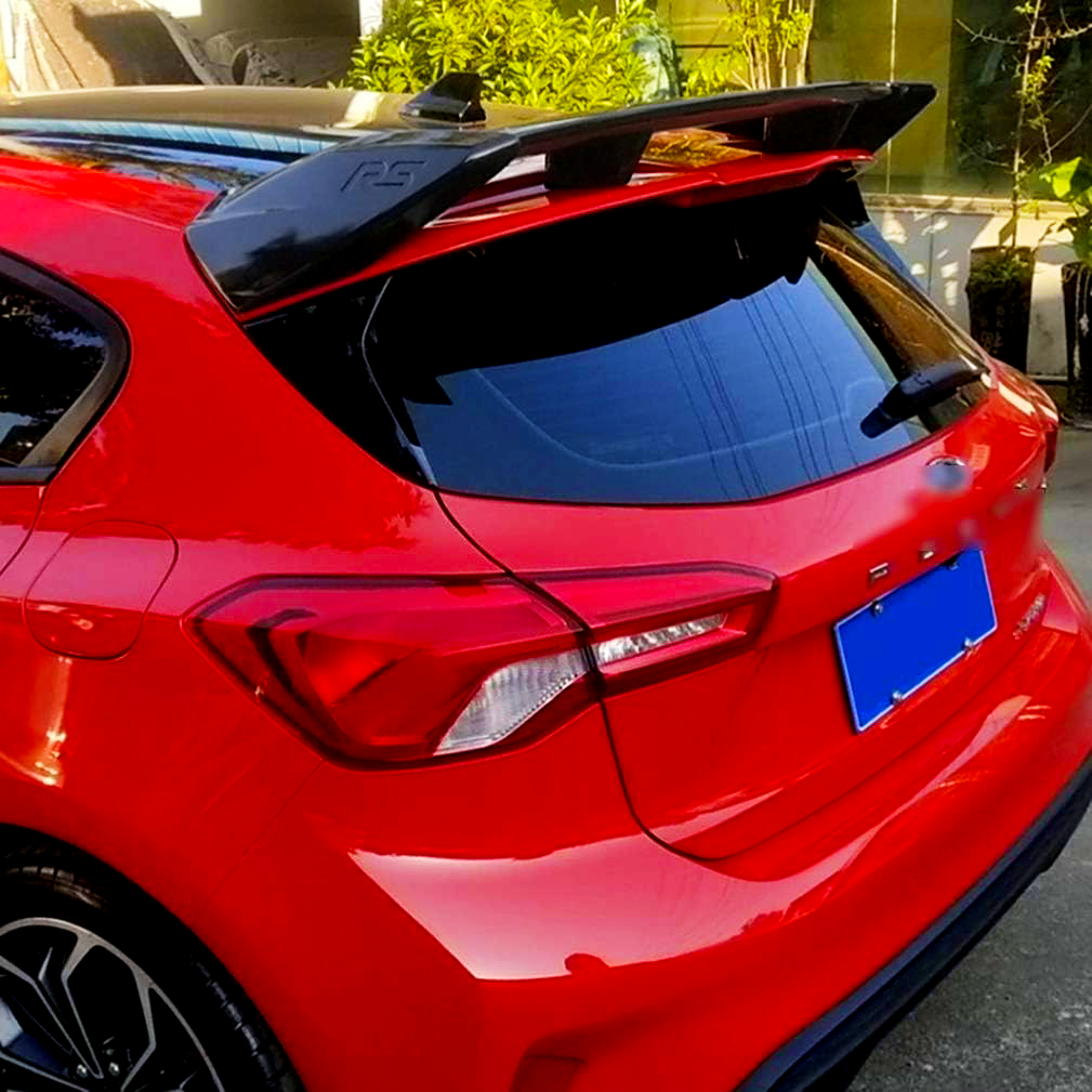 Red car with a prominent black spoiler labeled "RS," parked on a street beside a glass building and green shrubs, reflecting the surroundings on its glossy surface.