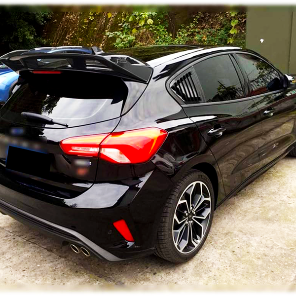 A sleek black hatchback car is parked on a concrete lot, surrounded by greenery and other vehicles. It features tinted windows, stylish taillights, and dual exhaust pipes.