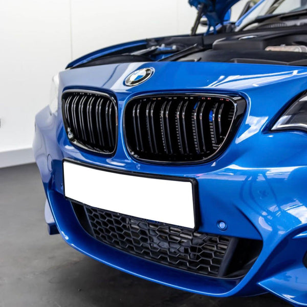 A blue car's front end with an open hood, featuring a kidney grille and blank license plate, in a garage setting.