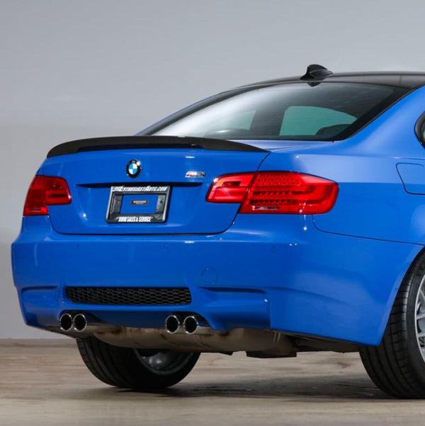 A blue BMW car is parked indoors, focused on its rear end with dual exhaust pipes. The license plate reads "www.forsale.com, BMW SALES SERVICE."