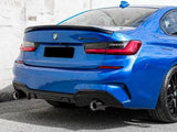 A blue BMW car is parked on a street, against a white wall. The model is identified as 