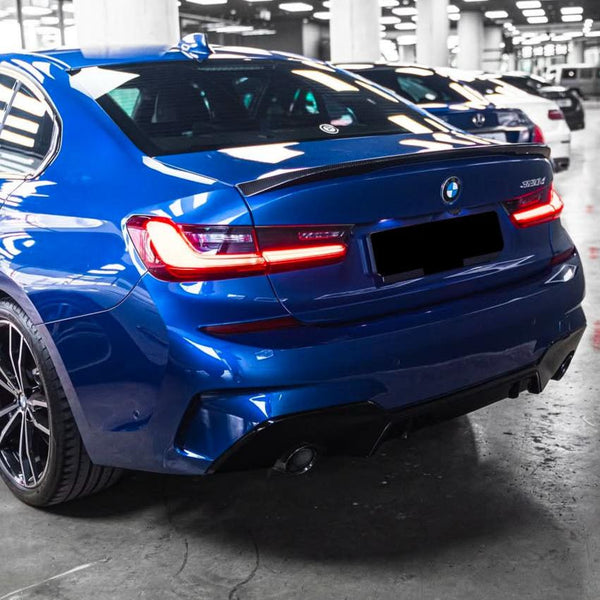 A blue BMW 320d with illuminated taillights is parked in an indoor garage alongside other vehicles, under bright overhead lights.
