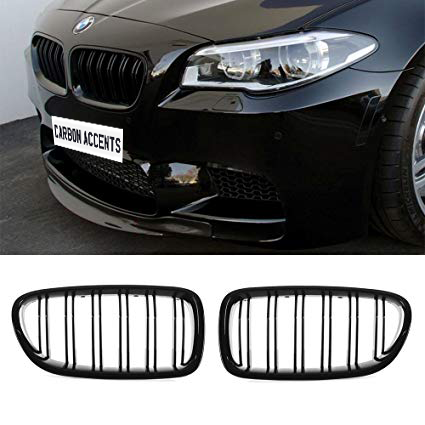 A black BMW car displays its front grille with a license plate reading "CARBON ACCENTS." Below are two separate black grille pieces, set against a white background.