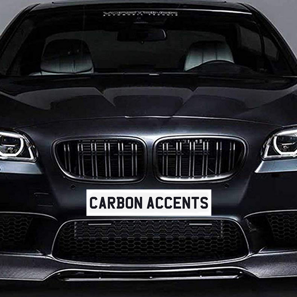 A black car with illuminated headlights sits in a studio setting. The license plate reads "CARBON ACCENTS." The car has a sleek, modern design.