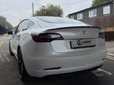A white Tesla car is parked on a street near residential buildings. Text reads 