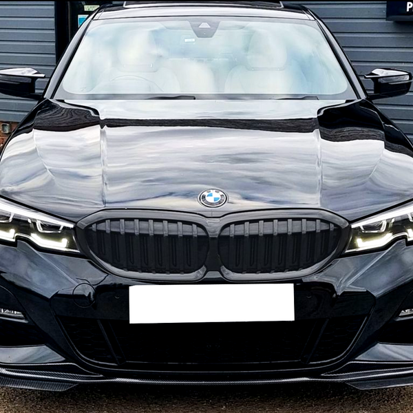 A black BMW car is parked, displaying its front grille and headlights. It is situated in a lot with a building in the background displaying the text "PROVIDER."