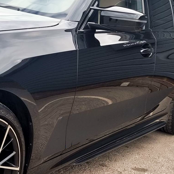 A shiny black car, parked in a lot, shows reflections on its side. The wheel displays tire specifications: "245/35 ZR20." A building wall is partially visible.