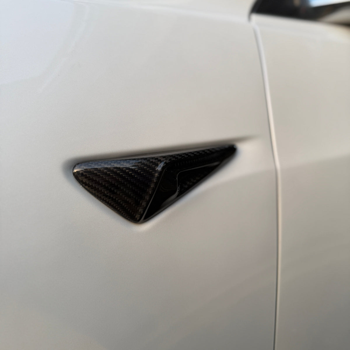 Carbon fiber triangular vent, embedded in a smooth white surface, showcasing contrasting textures on what appears to be a vehicle body exterior.