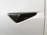 Carbon fiber trim piece, triangular in shape, embedded on a smooth, white vehicle surface. The trim adds a sleek, modern accent to the car's exterior design.