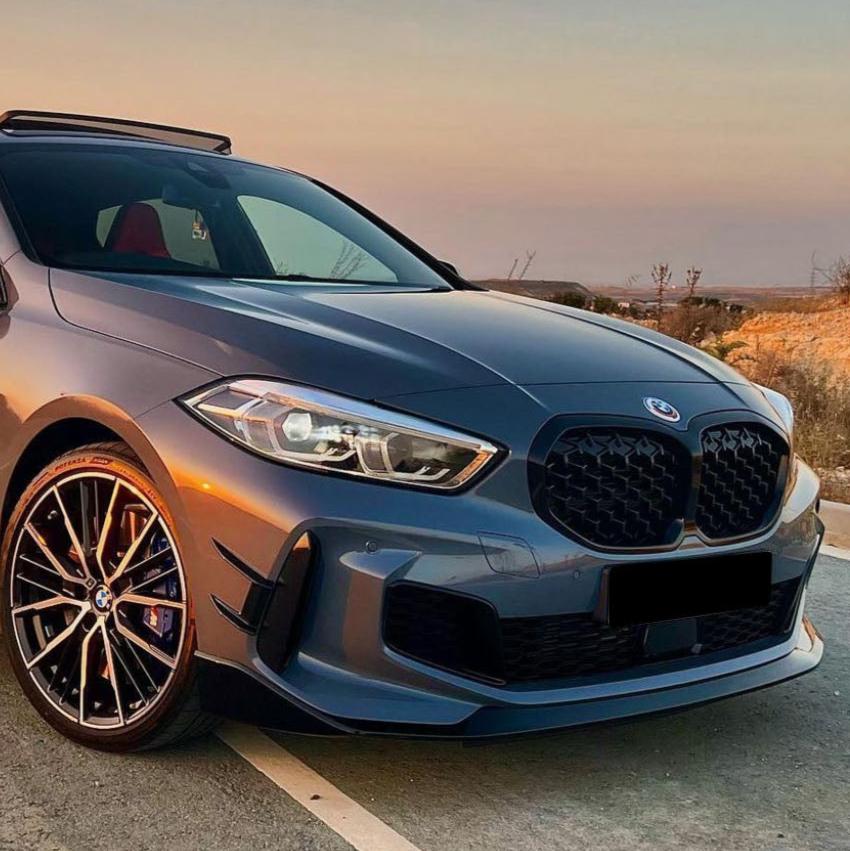 A modern, gray sports car is parked on a road at sunset, showcasing sleek lines and distinctive wheels, with a barren landscape in the background.