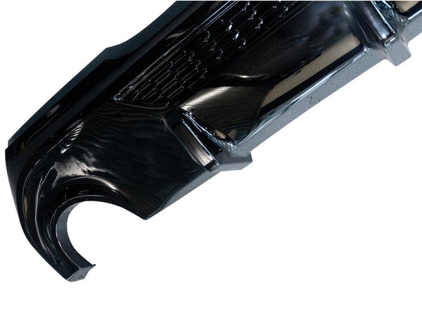 A glossy black car bumper with an intricate design is displayed against a plain white background, showcasing its sleek curvature and surface details.
