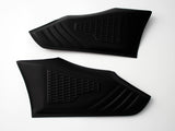 Two black rubberized grip pads lie flat, featuring textured patterns for grip enhancement, against a plain white background.