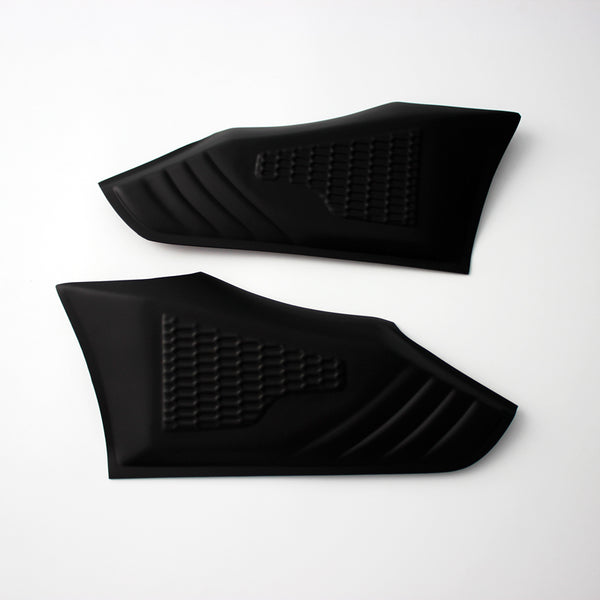 Two black rubberized grip pads lie flat, featuring textured patterns for grip enhancement, against a plain white background.