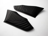 Two black rubber grip pads with textured patterns are placed on a light surface. Each pad features a distinct grid and ribbed design, typically used for vehicle or equipment grip enhancement.