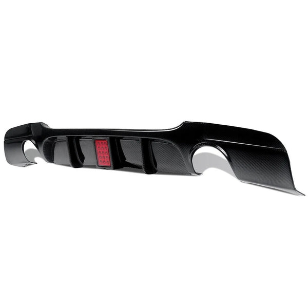 A black carbon fiber rear car diffuser with aerodynamic fins, featuring a small rectangular red light, placed against a white background.