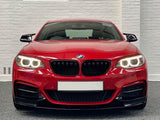 A red BMW car, headlights on, is parked indoors against a white brick wall backdrop.