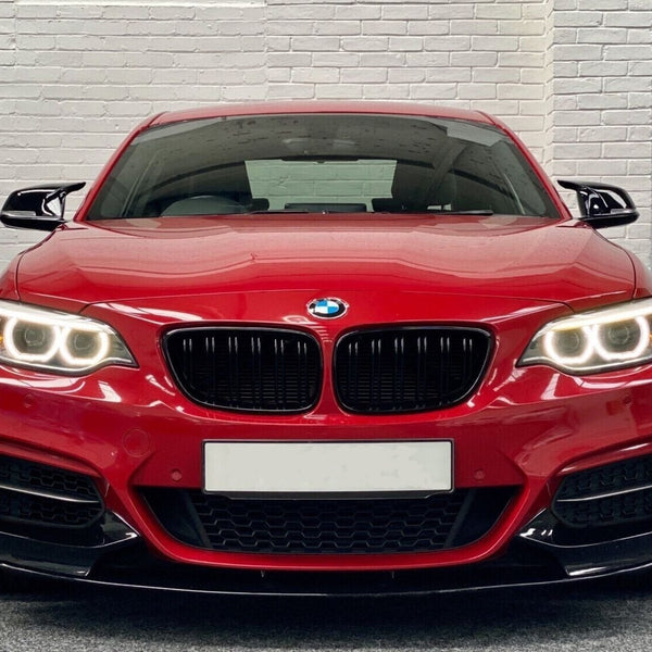 A red BMW car, headlights on, is parked indoors against a white brick wall backdrop.