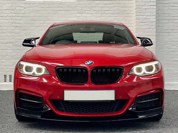 A red BMW car, headlights on, is parked indoors against a white brick wall backdrop.