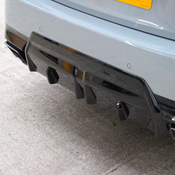 Car's rear features a glossy black diffuser with fins and exhaust openings, parked on a concrete surface. A yellow license plate is partially visible above.