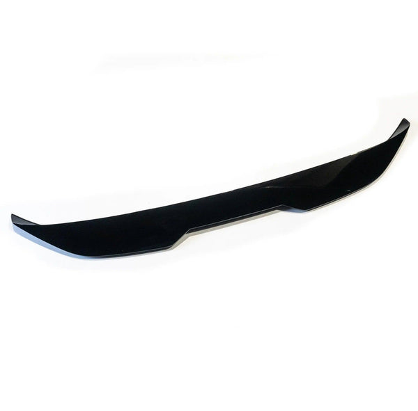 A sleek, black car front lip spoiler rests on a white background, featuring sharp edges and a subtle curvature designed to improve aerodynamics.