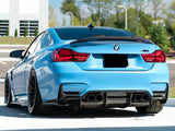 A blue BMW M4 car is parked on a paved surface with a modern building and greenery in the background.