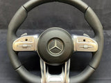 A black and silver steering wheel displays a prominent Mercedes logo at the center, surrounded by multifunctional buttons on the sides. 