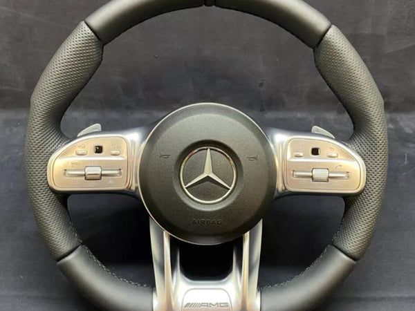 A black and silver steering wheel displays a prominent Mercedes logo at the center, surrounded by multifunctional buttons on the sides. "AIRBAG" and "AMG" are inscribed below.