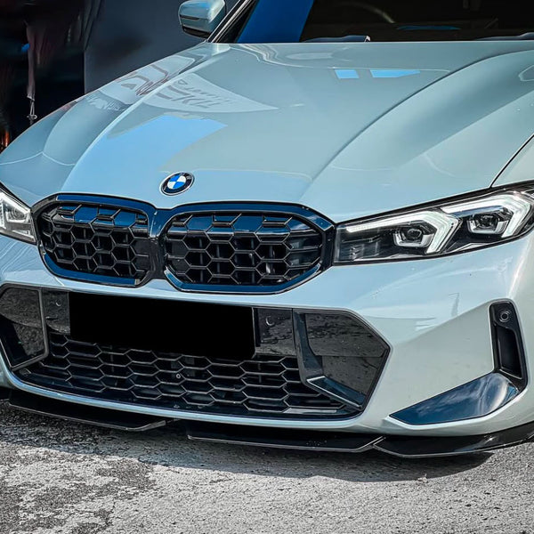Car front showcasing a sleek design; the BMW emblem is centered above a prominent black grille with hexagonal patterns. It's parked on asphalt with a blurred vehicle in the background.