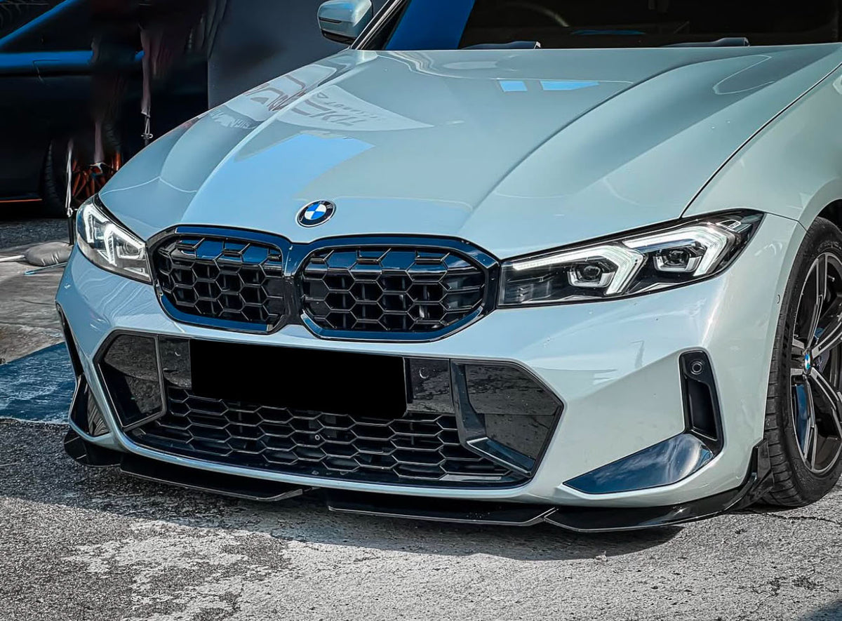 A white BMW car is parked, featuring a distinctive front grille and sleek headlights. It is situated on a paved surface with a darker vehicle partially visible in the background.