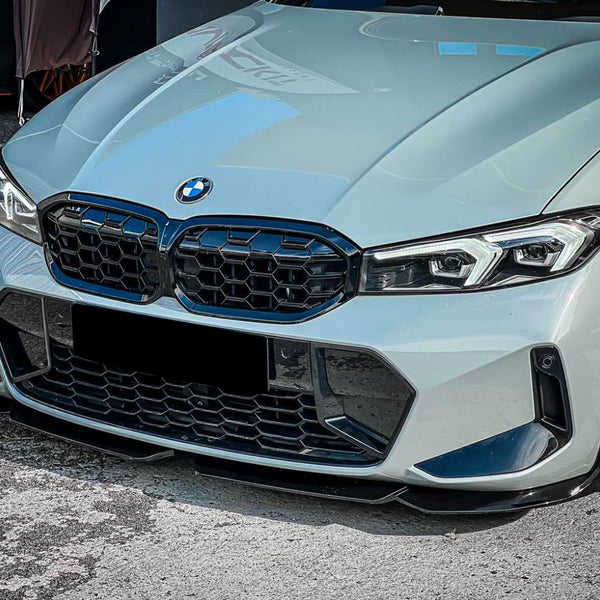 A sleek, gray BMW car's front view with a large grille and angular headlights, parked on a textured asphalt surface.