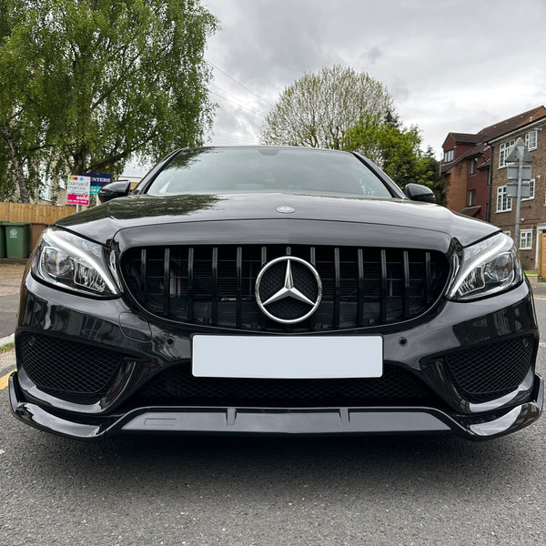 A black Mercedes-Benz car is parked on a suburban street near brick houses and green trees, with a real estate sign in the background.