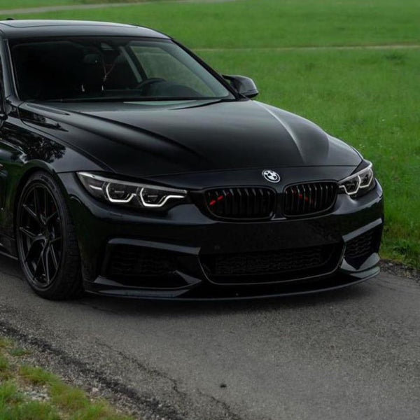 A sleek black car with distinct headlights is parked on a paved road, bordered by lush green grass in a calm, open area.