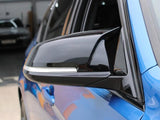 A sleek black side mirror is attached to a blue car, reflecting part of a garage interior, with cars and industrial elements in the background.