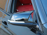 A sleek black car's side mirror reflects the sky and surroundings. The open window reveals red interior seats, set against an urban environment.