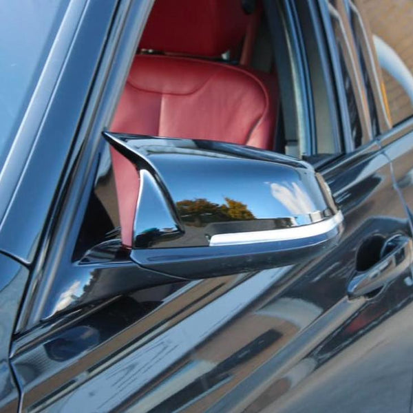 A sleek car side mirror reflects the sky and surroundings in a close-up shot, with a red leather car interior visible through the open window.