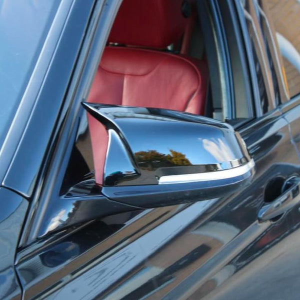 A black car door's side mirror reflects the sky and trees, positioned outside a vehicle with visible red leather interior. The context suggests an urban or suburban environment.