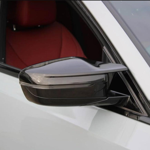 A sleek, black side mirror protrudes from a white car door, reflecting the surroundings. The car interior is visible with a red seat, suggesting a luxurious design.