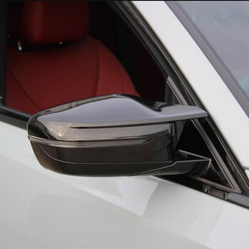 A black car side mirror is attached to a white vehicle. The window is open, revealing a red interior. The setting appears calm and focused on the vehicle's design features.