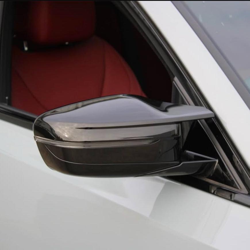 A glossy black side mirror is attached to a white car, with a visible red interior seat in the background.