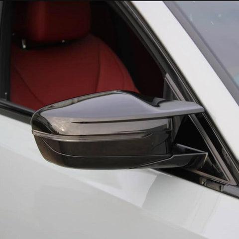 Side mirror with a sleek design attached to a white vehicle, facing outward. The interior features a red seat, visible through the window.