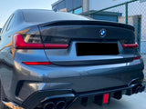 A dark BMW car parked near a fencing; its distinctive rear lights and dual exhausts stand out. The background includes a modern building under a clear sky.