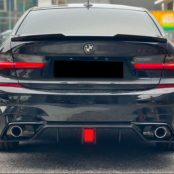 A black BMW 530i is parked, showing its rear view with illuminated taillights and dual exhausts. It's situated on a paved area near buildings.