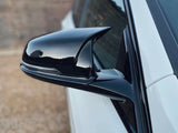 A black side mirror, attached to a white car, reflects the sky. The background features a blurred, earthy-colored surface with a textured pattern.