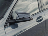 The side of a sleek car features a shiny side mirror reflecting clouds. The car's metallic surface also shows a mirror-like reflection, set outdoors under a bright sky.