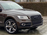 A brown Audi SUV is parked on a wet, textured pavement. It has shiny alloy wheels and distinctive front grille, set against a background of leafless trees and hedges.