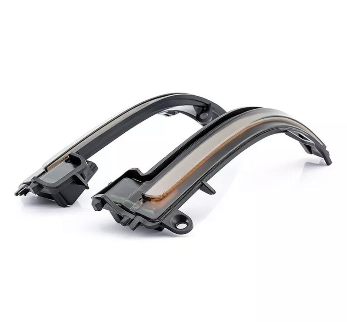 Curved black plastic car light indicators rest on a white surface, featuring a transparent cover housing internal amber LED strips.