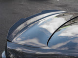 A shiny car roof reflects white clouds and blue sky, parked on a dark asphalt surface. The smooth surface emphasizes the car's sleek design.