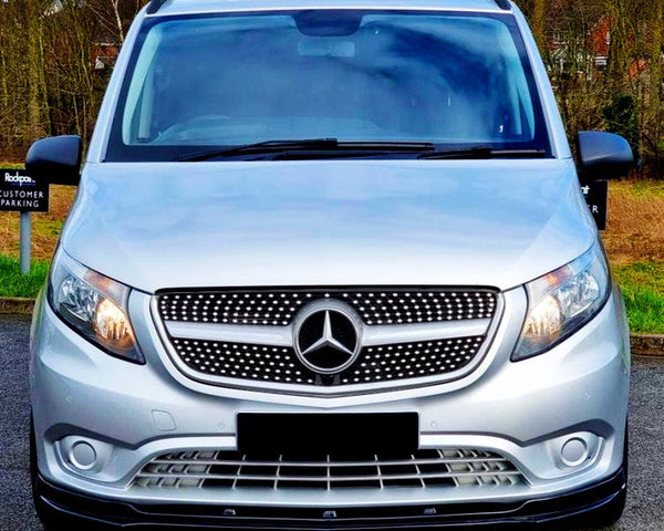 A silver van with a prominent Mercedes logo is parked on a road, surrounded by leafless trees and a grassy area. Signs read "Rodger's Customer Parking."