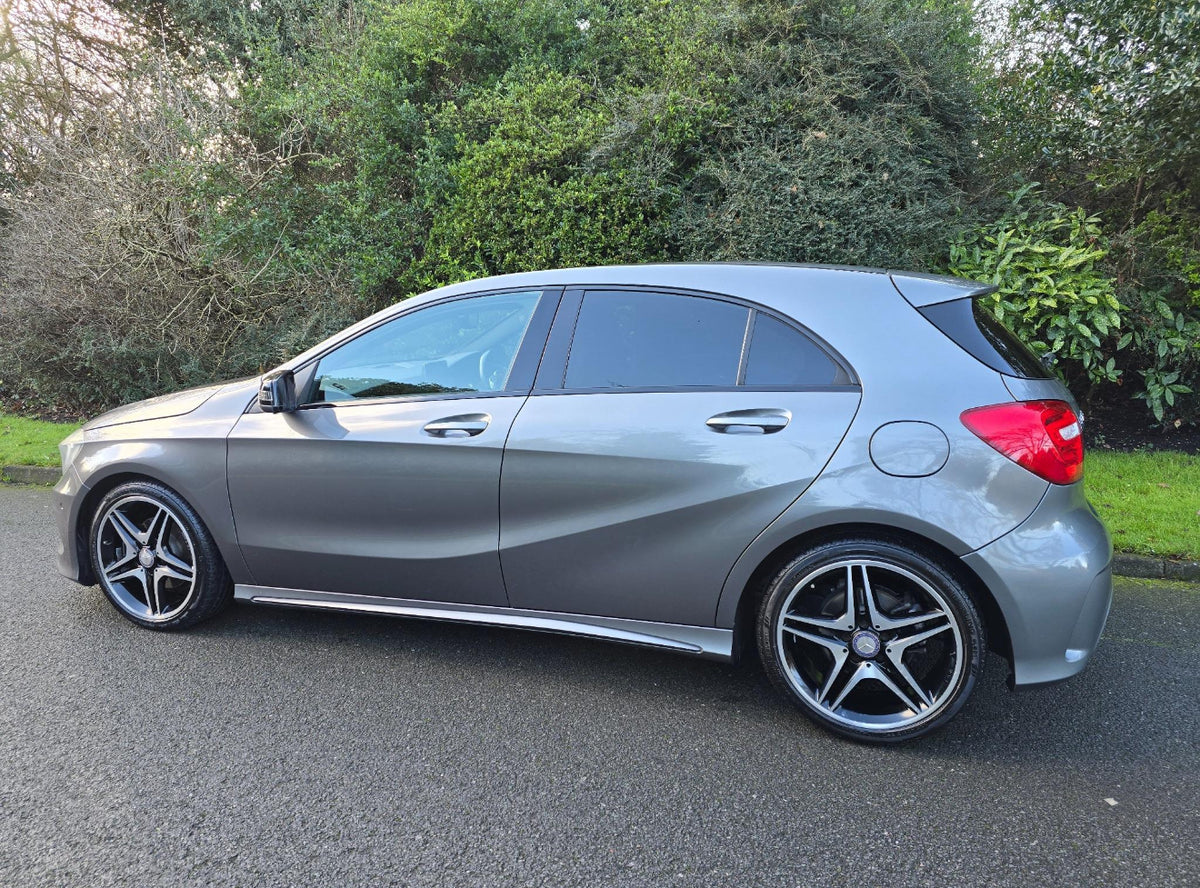 A silver car is parked on a road beside dense green bushes. It features sleek curves, dark-tinted windows, and modern, star-shaped alloy wheels.