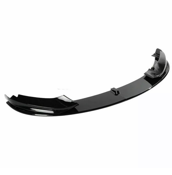A sleek, black car front lip spoiler is resting on a plain, white background. It features a curved aerodynamic design, often used for reducing drag and enhancing vehicle performance.